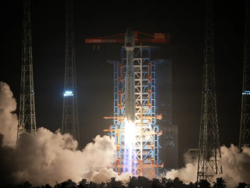 A Long March 8A rocket lifts off at night from the Hainan Commercial Space Launch Center, with bright flames and exhaust clouds illuminating the launch tower and surrounding gantry structures.
