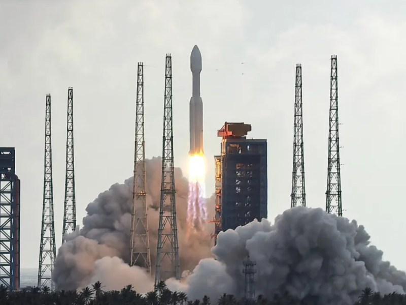 A Long March 8A rocket lifts off from the Hainan Commercial Space Launch Center in southern China, sending a batch of Guowang broadband satellites into orbit. The rocket rises through a cloud of exhaust and smoke, framed by tall metal service towers under a bright sky.