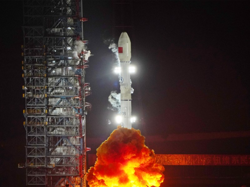 A Long March 3B rocket launches ChinaSat-9C from Xichang Satellite Launch Center at night, with flames and smoke billowing from the base and the illuminated rocket lifting off against a dark sky.